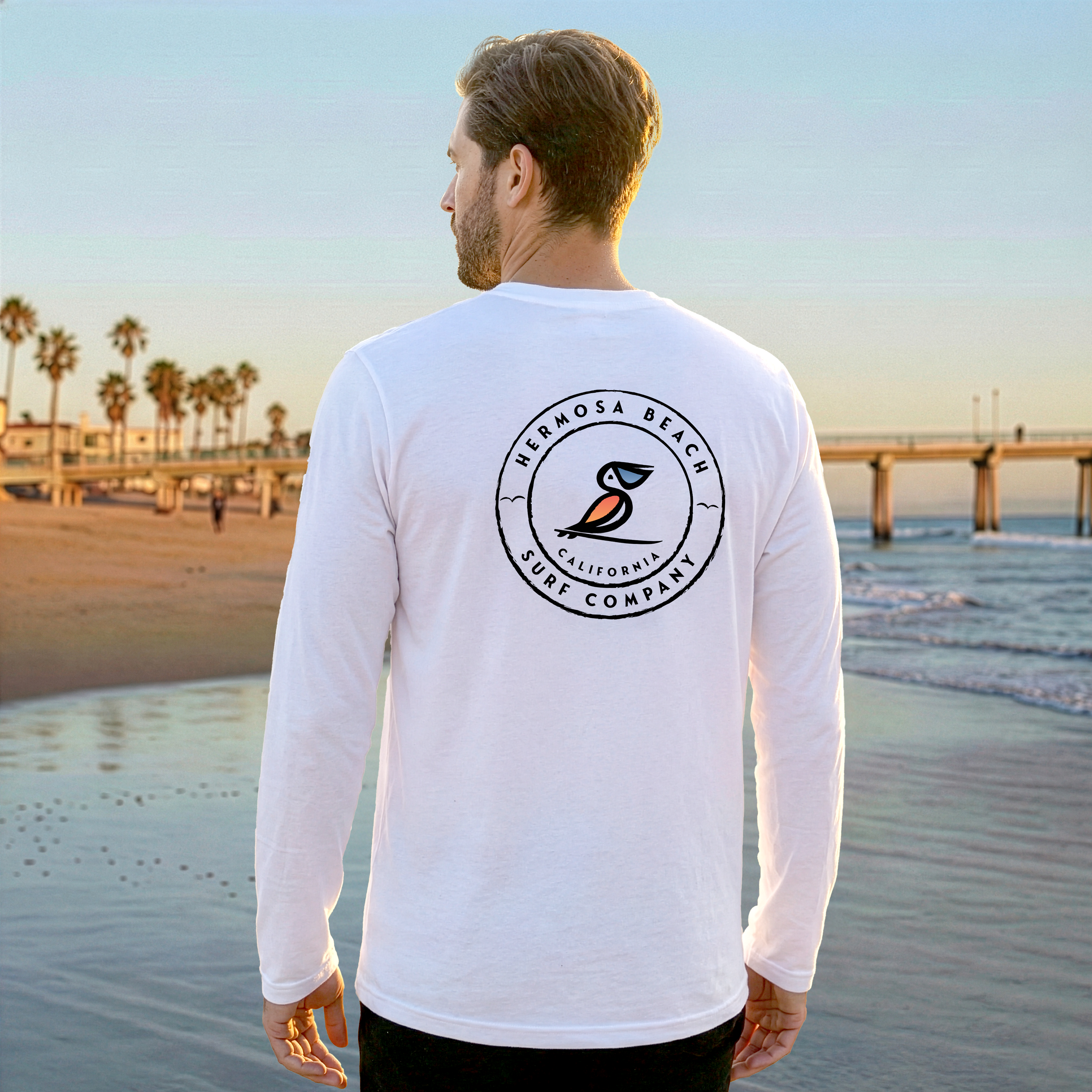 Man wearing a white long-sleeve shirt with a logo on the beach