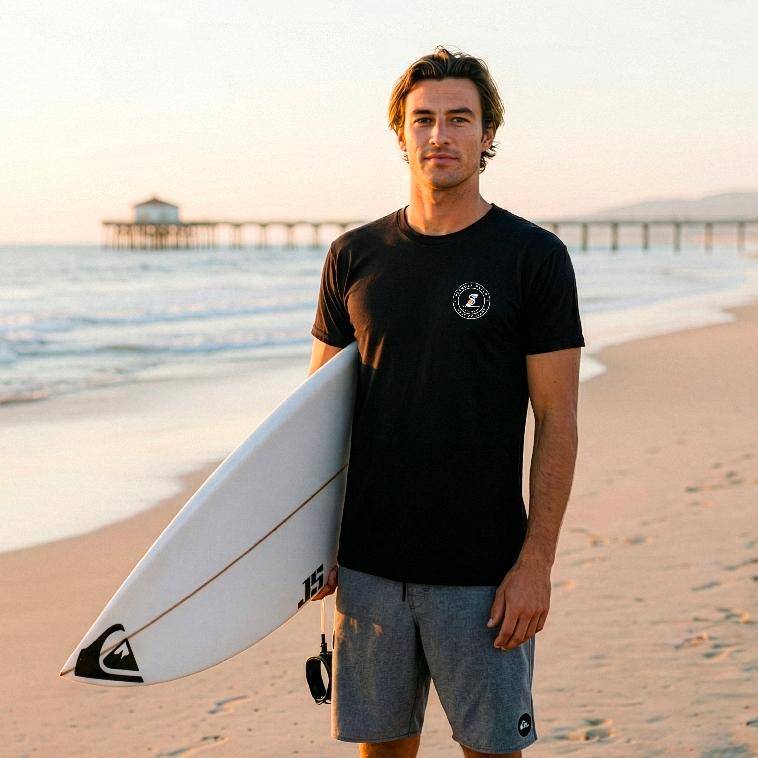 Man holding a surfboard on a beach with a pier in the background