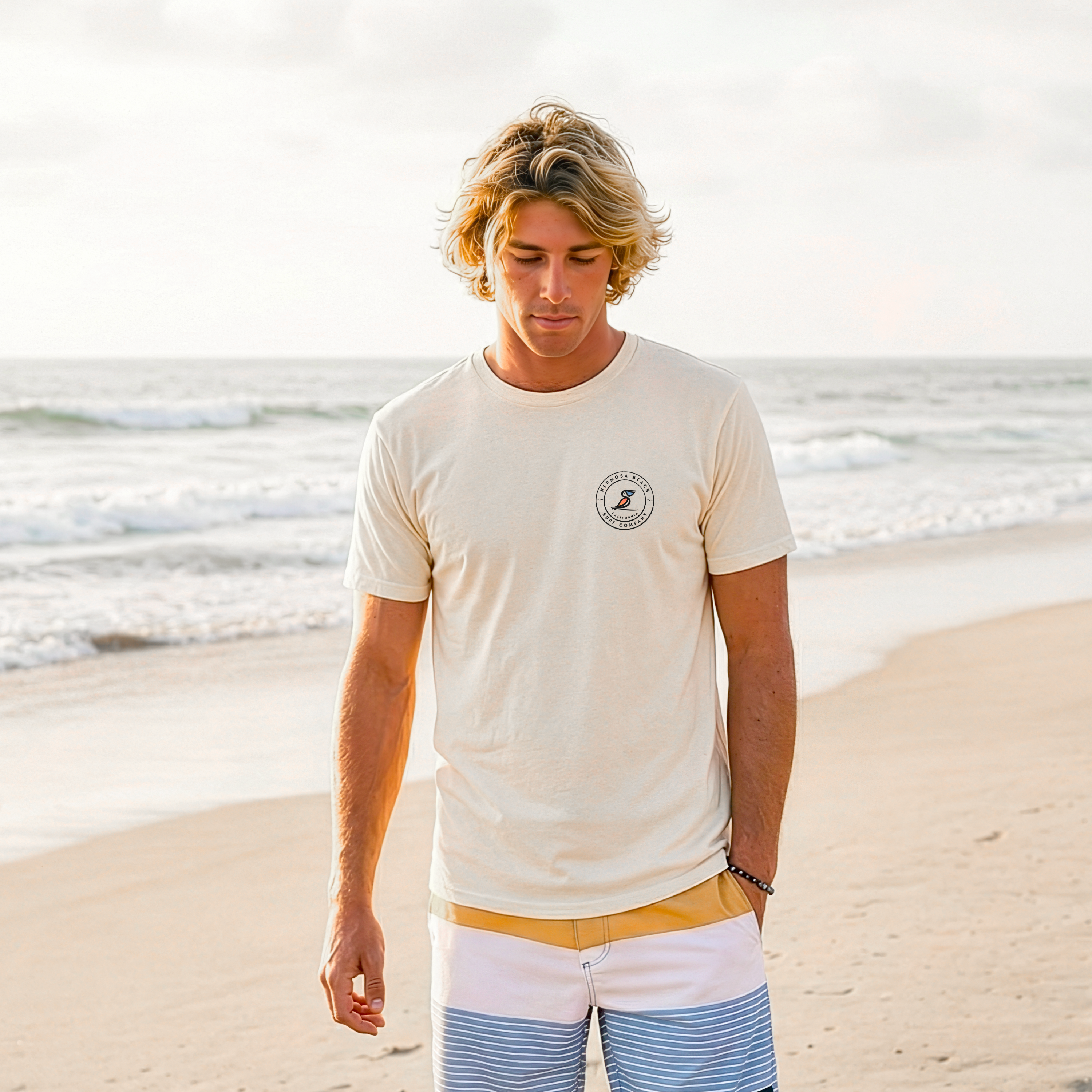 Man standing on a beach wearing a Cream t-shirt with a logo and striped shorts.