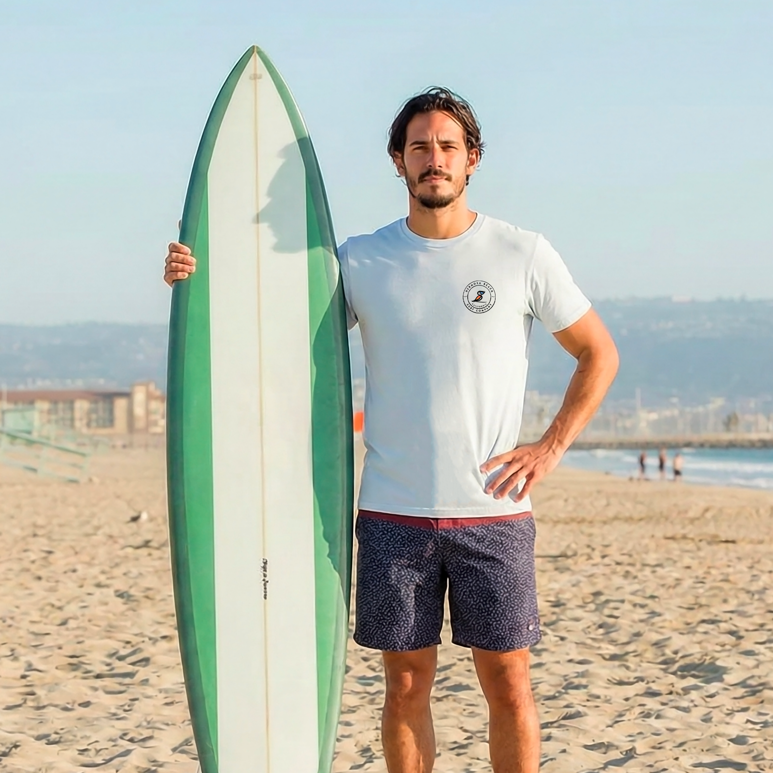Man holding a green and white surfboard on a beach