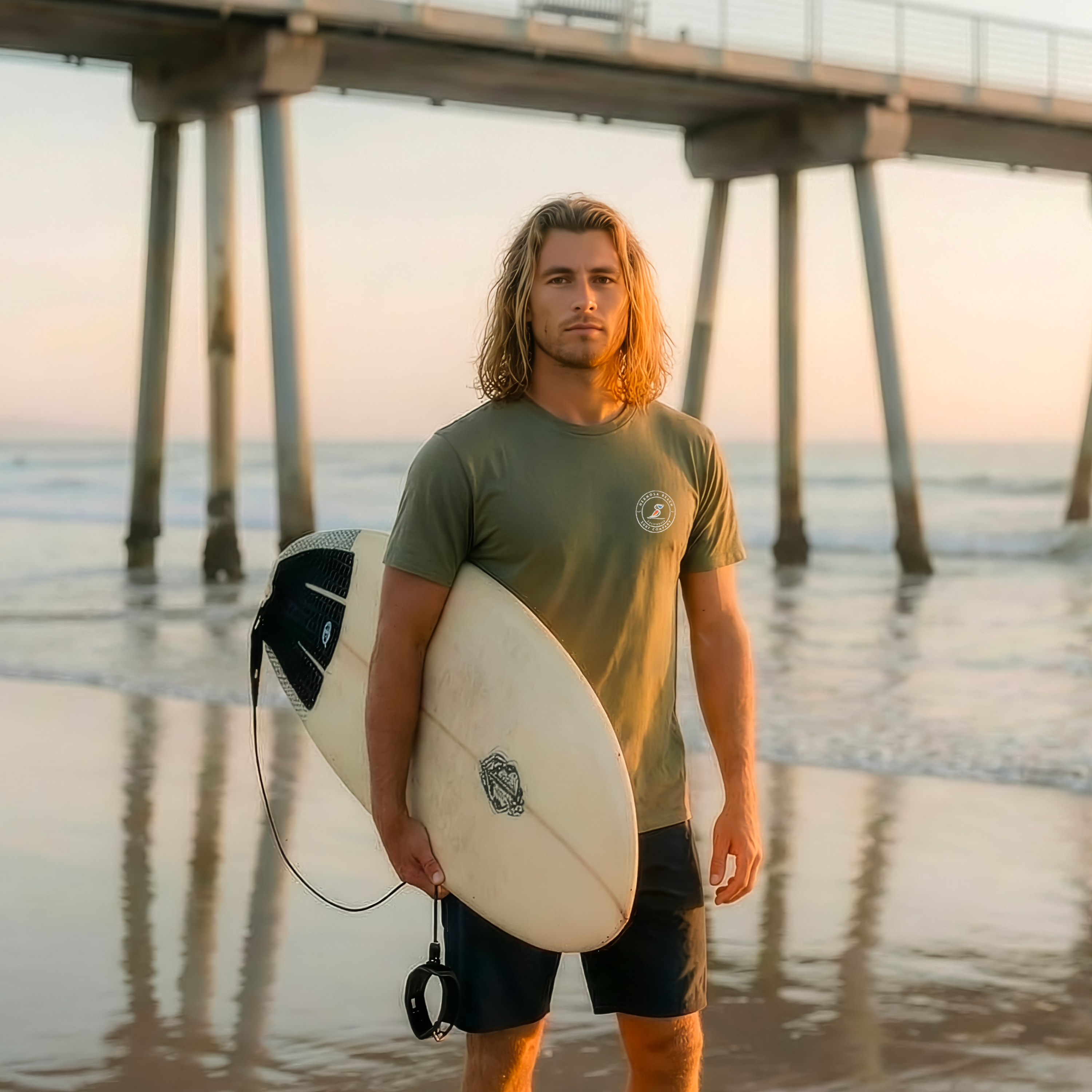 Man holding a surfboard on a beach with a pier in the background