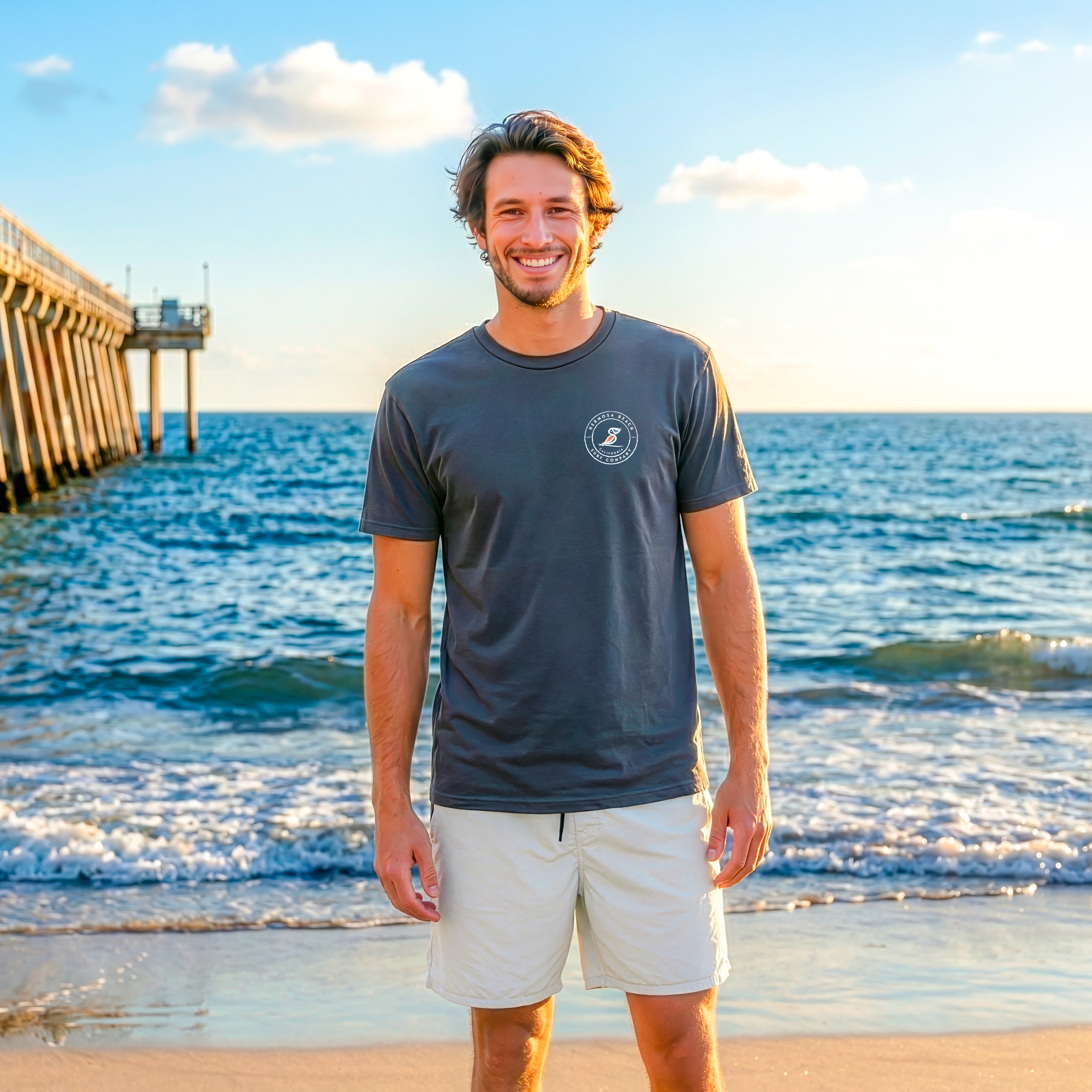 Man standing on a beach wearing a Vintage Black t-shirt and light-colored shorts, with a pier and ocean in the background.