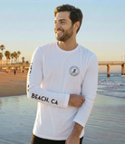 Man wearing a white long-sleeve shirt with 'Beach, CA' text on a beach background