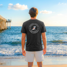Man wearing a black t-shirt with a logo on the beach