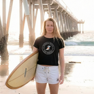Woman holding a surfboard on a beach with a pier in the background
