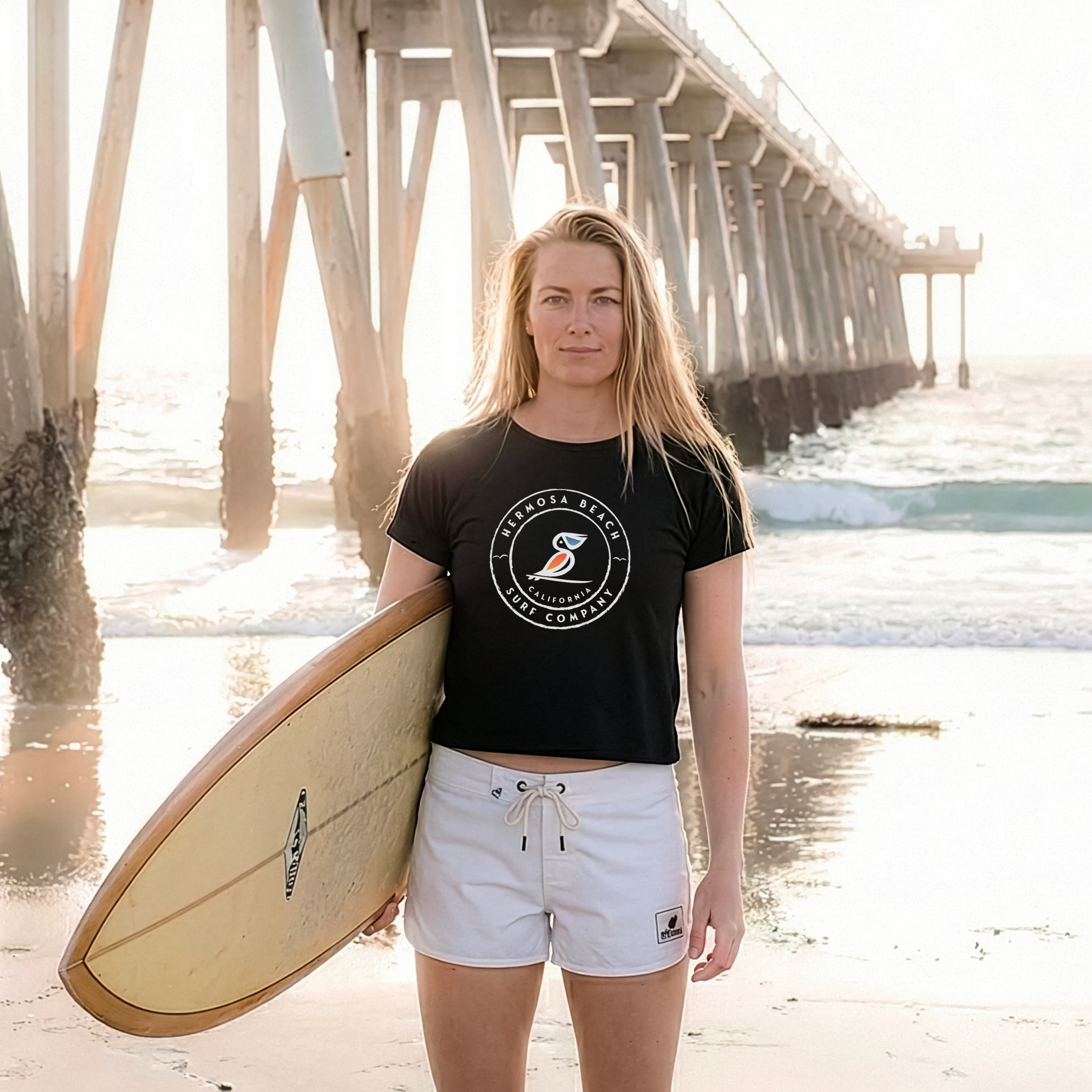 Woman holding a surfboard on a beach with a pier in the background