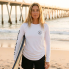 Woman holding a surfboard on a beach with a pier in the background